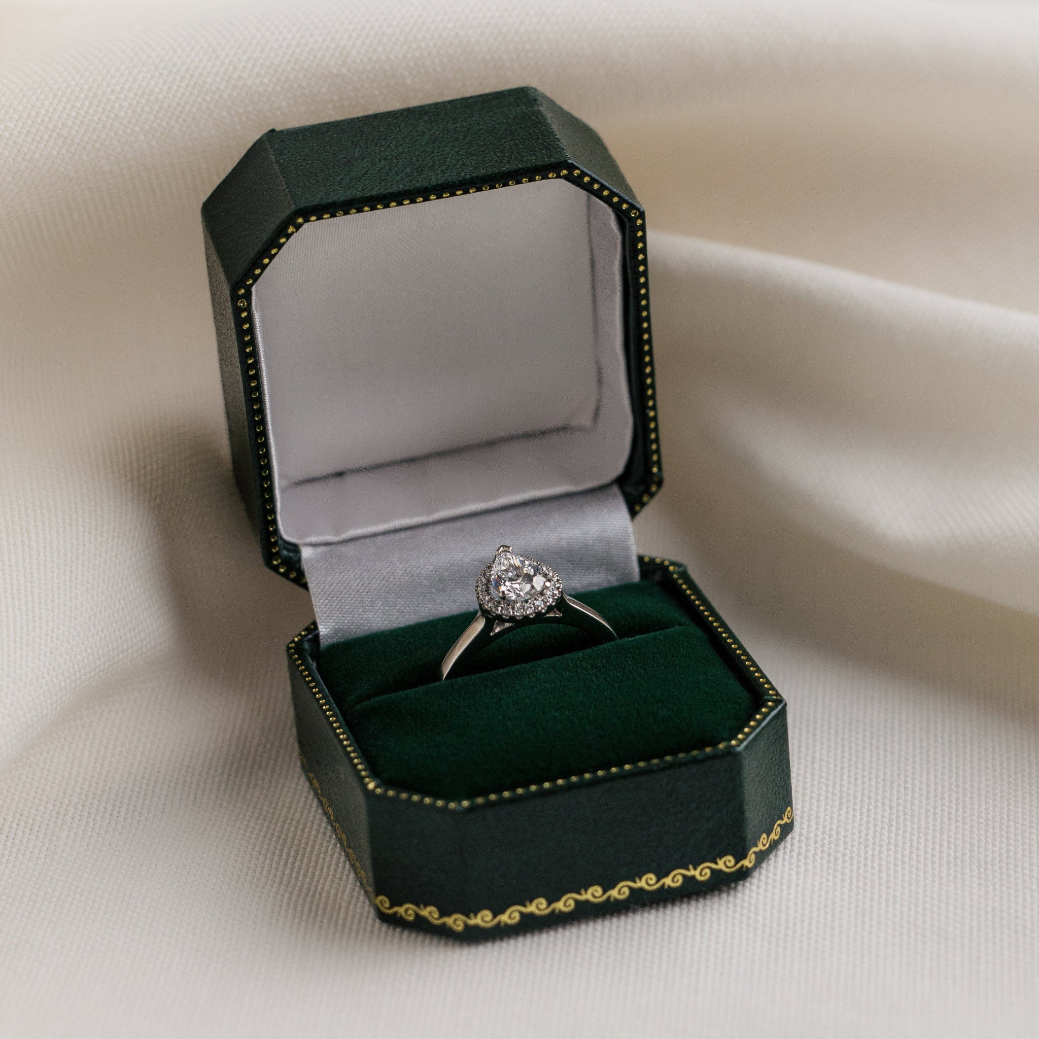Diamond ring in a green jewelry box on a white fabric background