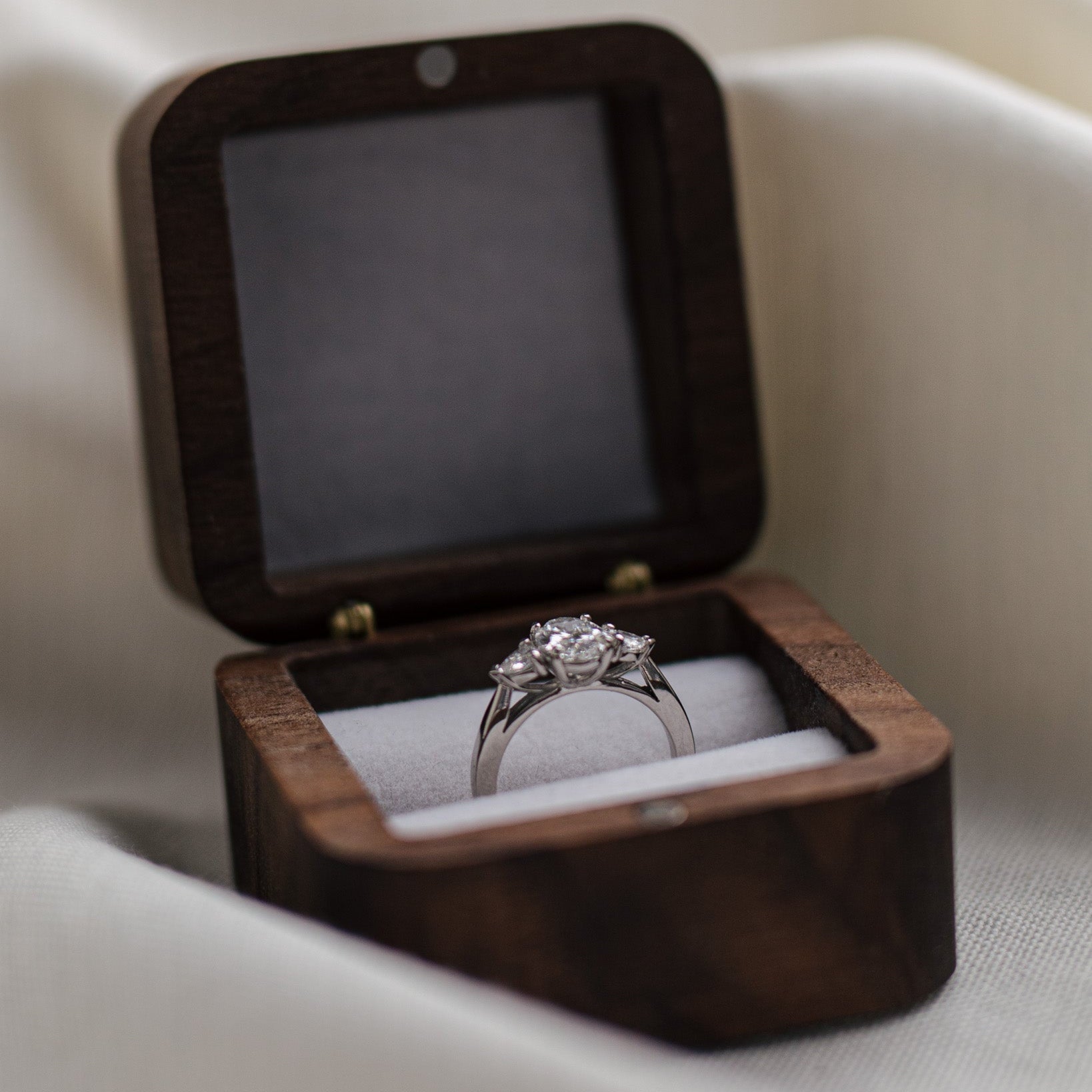 Diamond ring with a diamond in an open wooden box on a light fabric background